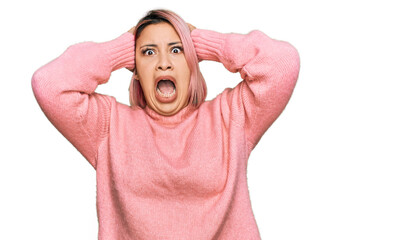 Hispanic woman with pink hair wearing casual winter sweater crazy and scared with hands on head,...