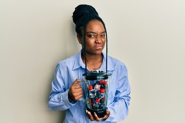 African american woman with braided hair holding food processor mixer machine with fruits skeptic and nervous, frowning upset because of problem. negative person.