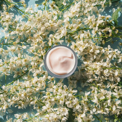 Cosmetic cream jar on the background of white small spring flowers of Byttneria. Natural organic cosmetics concept. Top view, flat lay