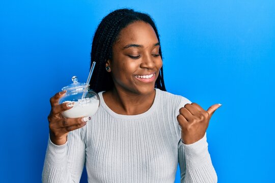African american woman with braided hair holding bowl of sugar candy pointing thumb up to the side smiling happy with open mouth