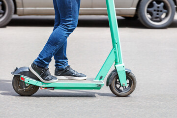 A modern concept on mobile electric transport: a person rides an electric scooter along the carriageway of a city street. - obrazy, fototapety, plakaty