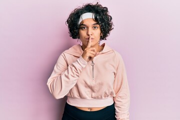 Fototapeta na wymiar Young hispanic woman with curly hair wearing sportswear asking to be quiet with finger on lips. silence and secret concept.