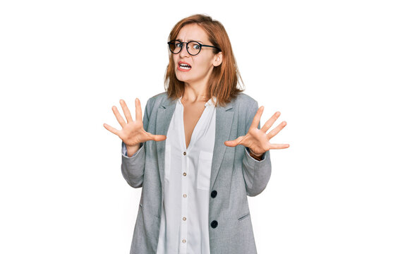 Young caucasian woman wearing business style and glasses afraid and terrified with fear expression stop gesture with hands, shouting in shock. panic concept.