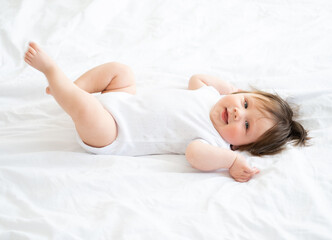 healthy 6 month baby boy smiling and lying on a white bedding at home.