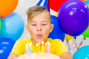 Fototapeta na wymiar Teen boy celebrates his birthday and blows candles on cake. Empty space for text