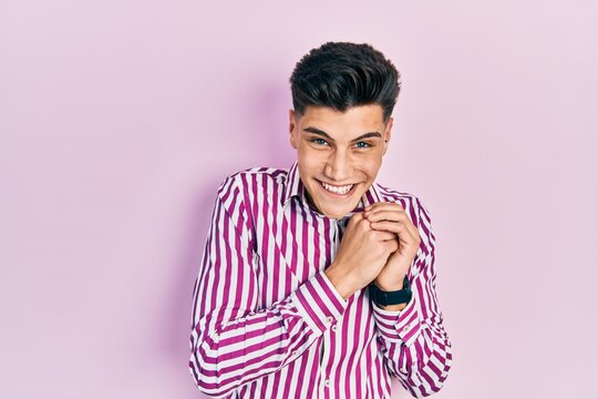 Young hispanic man wearing casual clothes laughing nervous and excited with hands on chin looking to the side