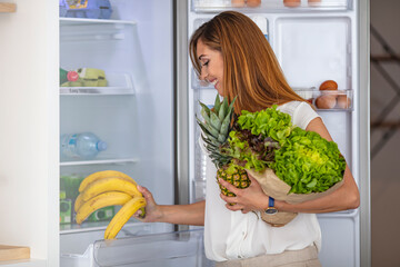 Happy young woman standing at the opened fridge. Portrait of cute serious female standing near open...