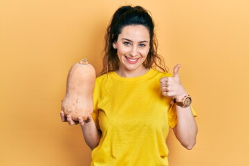 Young hispanic woman holding healthy fresh pumpkin smiling happy and positive, thumb up doing excellent and approval sign