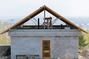 Obraz premium Construction of a private house from foam concrete blocks. Wooden rafters of a triangular roof, chimney. Background - city, sky.
