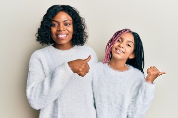 Beautiful african american mother and daughter wearing casual winter sweater pointing to the back behind with hand and thumbs up, smiling confident