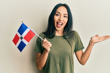 Young hispanic girl holding dominican republic flag celebrating achievement with happy smile and...