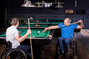 Adult men with disabilities in a wheelchair play billiards in the club