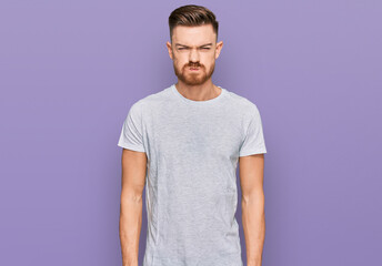 Young redhead man wearing casual grey t shirt puffing cheeks with funny face. mouth inflated with air, crazy expression.