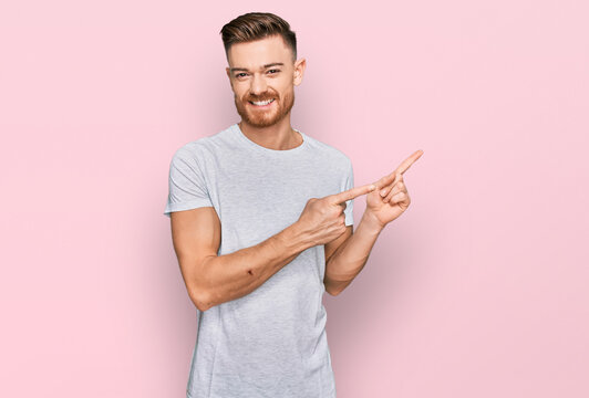 Young Redhead Man Wearing Casual Grey T Shirt Smiling And Looking At The Camera Pointing With Two Hands And Fingers To The Side.