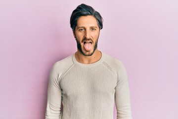 Young hispanic man wearing casual winter sweater sticking tongue out happy with funny expression. emotion concept.