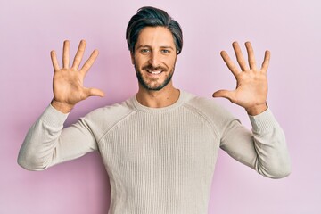 Young hispanic man wearing casual winter sweater showing and pointing up with fingers number ten while smiling confident and happy.