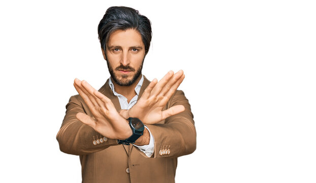 Young hispanic man wearing business clothes rejection expression crossing arms and palms doing negative sign, angry face