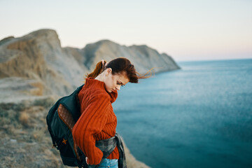woman in a sweater with a backpack walks in nature in the mountains near the sea