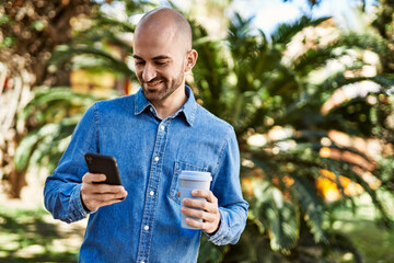 Fototapeta premium Young hispanic man using smartphone and drinking coffee at the park.