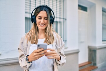 Naklejka premium Young caucasian woman smiling happy using smartphone and headphones at the city.