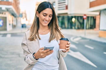 Young caucasian woman smiling happy using smartphone and drinking take away coffee at the city.