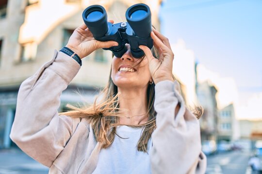 Young caucasian woman smiling happy looking for new opportunity using binoculars walking at the city.