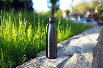Stainless thermo water bottle of black on background of green grass. Reusable bottles; zero waste;...