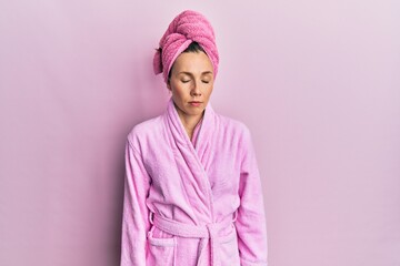 Fototapeta premium Young blonde woman wearing shower towel cap and bathrobe looking sleepy and tired, exhausted for fatigue and hangover, lazy eyes in the morning.