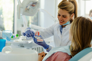 Young beautiful female doctor is showing to young female patient how to brush teeth properly.