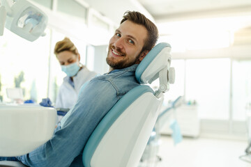 Happy young man sitting in dental chair, posing before examination and looking at the camera.