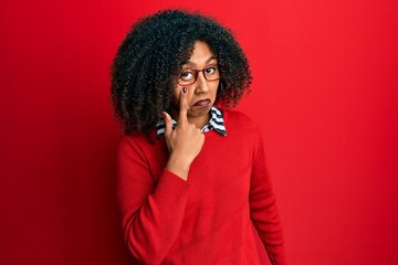 Beautiful african american woman with afro hair wearing sweater and glasses pointing to the eye watching you gesture, suspicious expression