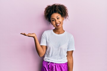 Beautiful african american woman with afro hair wearing sportswear smiling cheerful presenting and pointing with palm of hand looking at the camera.