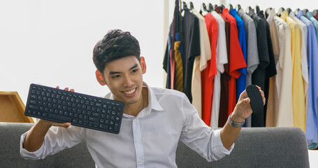 Asian man blogger broadcasting a video for selling product online such as Hats, shoes, headphones, clothing, safety headers.Shopping online concept and payment with credit card  at home