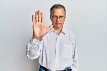 Middle age indian man wearing casual clothes and glasses doing stop sing with palm of the hand. warning expression with negative and serious gesture on the face.