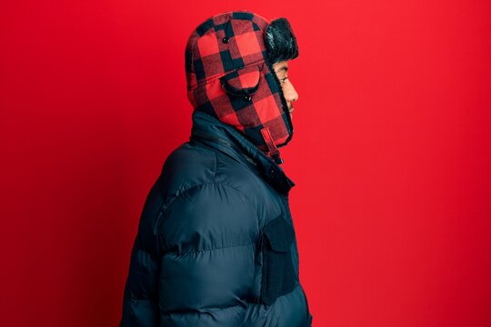 Young african american man with beard wearing winter hat and coat looking to side, relax profile pose with natural face with confident smile.
