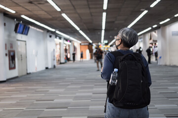 Behind Asian Senior smart woman traveler hipster wear medical facemask prevent COVID-19 virus disease with backpack standing look Walkway at airport terminal for boarding flight while Corona pandemic