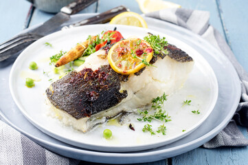 Modern style traditional roasted halibut fish filet with lettuce and lemon slices served as close-up on a design plate with copy space