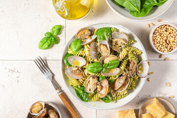Seafood pasta with vongole clams, spinach, parmesan cheese, pine nuts and basil in a plate with fork and knife. top view