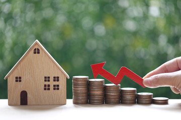 Mortgage,Woman hand holding red arrow graph and stack of coins money with model house on natural green background,Business investment and real estate concept