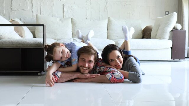 Young caucasian family with small daughter pose relax on floor in living room, smiling little girl kid hug embrace parents, show love and gratitude, rest at home together.
