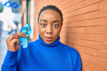 Young african american woman smiling happy holding blue awareness ribbon at the city.