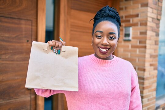 Young african american woman smiling happy holding delivery paper bag with take away food at the city.