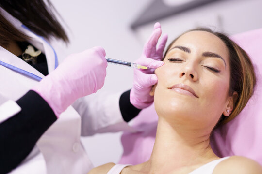 Doctor injecting hyaluronic acid into the cheekbones of a woman as a facial rejuvenation treatment.