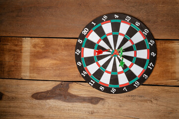 Close up shot red and green darts arrows in the target center on old wood background.