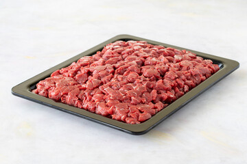 Chopped raw veal meat cubes for saute on white wooden table.