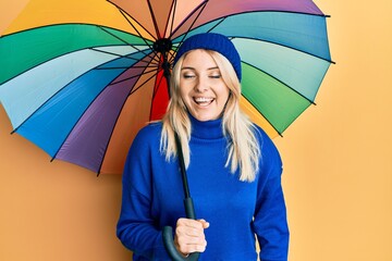 Young caucasian woman holding colorful umbrella smiling and laughing hard out loud because funny...