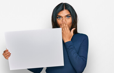 Young latin transsexual transgender woman holding blank empty banner covering mouth with hand,...