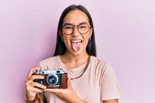 Young asian woman holding vintage camera sticking tongue out happy with funny expression.