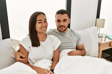 Fototapeta premium Young latin couple smiling happy hugging on the bed at home.