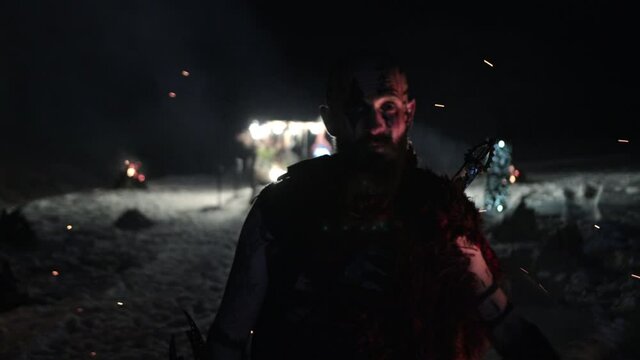 Viking is a brutal male warrior of dangerous appearance waiting for the enemy near fire. Concept of ancient traditions wild life barbarian conquerors. Low lighting, night.